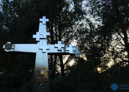 Wyróżniający się metalowy krzyż na ciemnym tle lasu, przy zachodzie słońca